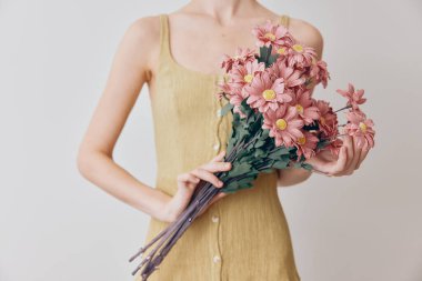 Sarı elbiseli kadın beyaz arka planda pembe kasımpatı buketi tutuyor..