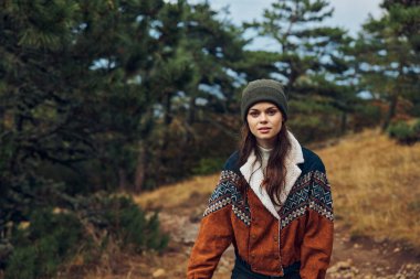 Şık şapkalı ve ceketli genç bir kadın huzurlu bir orman yolunda doğanın güzelliğini keşfediyor.