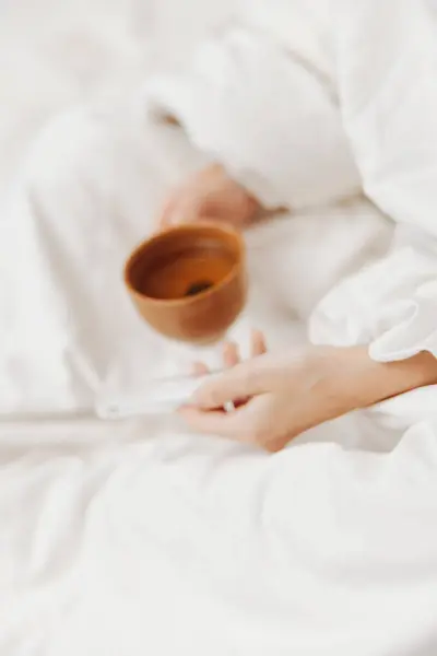 stock image Person lying in bed with a bowl of tea and a cup of water, next to another person holding a cup of tea and a bowl of water.