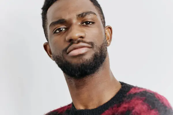 stock image A confident young man with a beard in a red sweater gazes directly at the camera, exuding self-assurance in a relaxed setting.