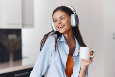 Evde huzurlu bir sabah boyunca mutfakta kulaklık ve kahveyle müzik seven bir kadın.