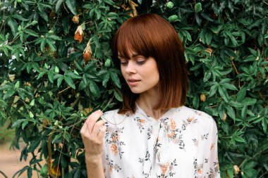 Canlı kızıl saçlı, yemyeşil çalıların önünde olgun bir elma tutuyor.