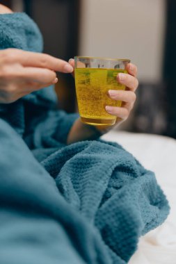 Mavi battaniyeli kadın otel yatağında bir bardak yeşil çay tutuyor..
