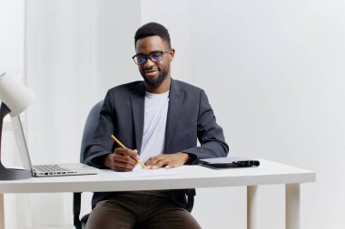 Kendinden emin Afro-Amerikan işadamı, üretken bir iş gününe hazır bir dizüstü bilgisayarla masasına fikirler yazıyor..