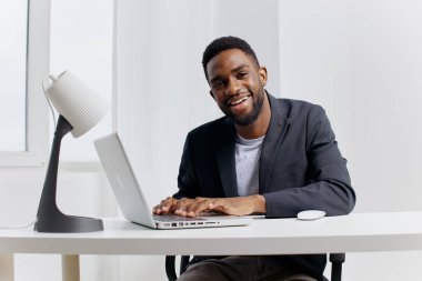 Neşeli bir Afro-Amerikan profesyonel şık, modern bir ofis masasında özenle dizüstü bilgisayarla çalışıyor..