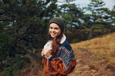 Mutlu genç bir kadın sonbahar ormanında güneşli bir günün tadını çıkarıyor. Etrafı renkli yapraklar ve ağaçlarla çevrili. Doğada gülümseyen güzelliğin portresi.