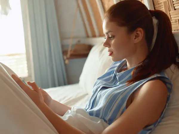 stock image A woman in comfortable loungewear lays on her bed, texting on her cell phone, showcasing a moment of relaxation at home.