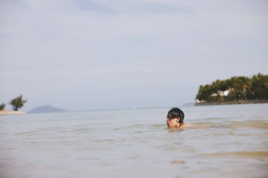 Gülümseyen adam, berrak mavi okyanusla çevrili ve palmiye ağaçlarıyla kaplı tropikal bir plaj cennetinde ferahlatıcı bir yüzüşten zevk alıyor..