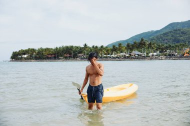 Mutlu Asyalı Adam Tropikal Sahilde Kano Macerasının tadını çıkarıyor