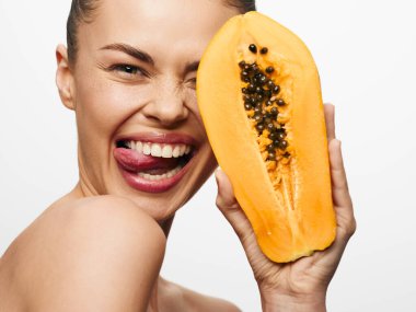 Yüzünün önünde olgun bir papaya tutan, küstah bir tavırla dilini çıkaran oyuncu bir kadın.