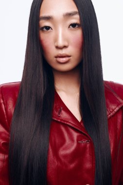 Uzun siyah saçlı, kırmızı deri ceketli şık bir genç kadın şehir ortamında bir fotoşopa poz veriyor.