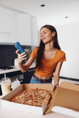 Yemek ve teknoloji konsepti için elinde bir dilim pizzayla telefonuyla fotoğraf çeken bir kadın.