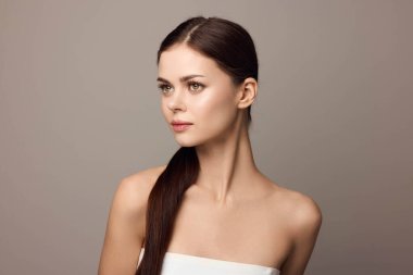 Uzun kahverengi saçlı, beyaz elbiseli güzel bir kadının portresi. Gri bir arka plana bakıyor..