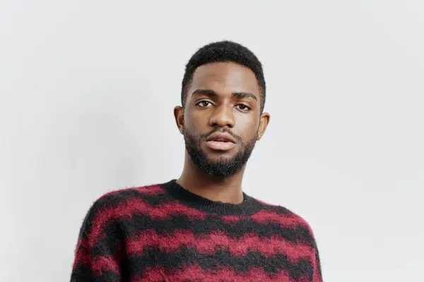 stock image Confident man in a red and black sweater poses effortlessly against a minimalist white wall, radiating style and charisma.