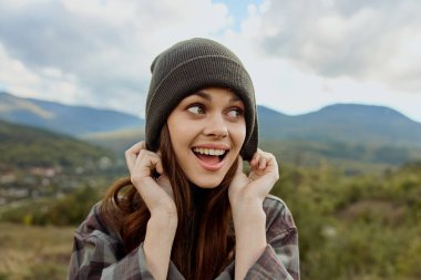 Şapkalı, ekose gömlekli şık bir kadın. Gülümsüyor ve moda portresi konseptiyle kameraya bakıyor.