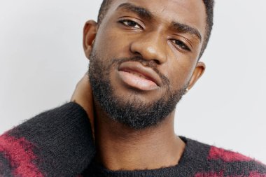 Modern kırmızı ve siyah süveterli, kendine güvenen sakallı adam, sade bir arka plan, canlı bir tarz ve karizmaya karşı duruyor..