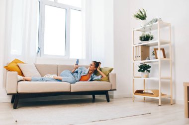 Evde Rahatlama: Oturma odasında Cozy Sofa 'da Gülümseyen ve Cep Telefonu Tutan Genç Kadın