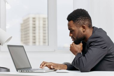 Modern bir ofiste çalışan, evrak işleri ve ofis malzemeleriyle çevrili, odaklanmış Afro-Amerikan bir iş adamı..