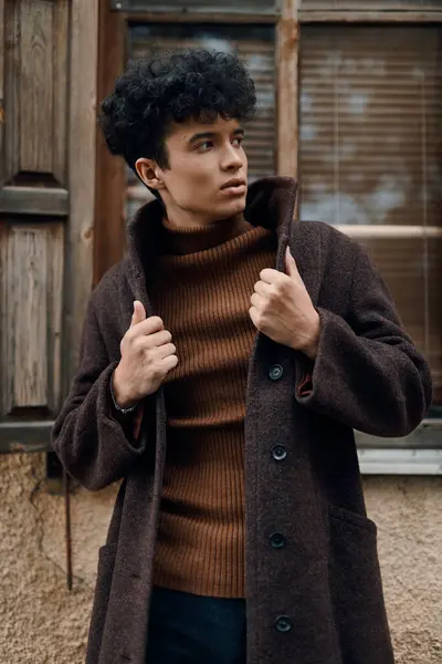 stock image Fashion photo of a young man in a brown coat and black turtleneck sweater standing in front of an old building.