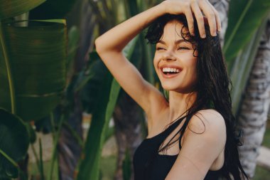 Güneşli bir günde arka planda palmiye ağacıyla ağacın önünde duran mutlu kadın.