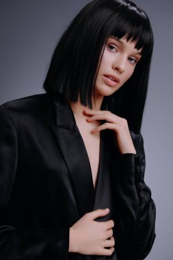 Siyah takım elbiseli kadın, elleri kalçasında, yan tarafa bakıyor, güçlü ve iddialı profesyonel bir tutum sergiliyor.