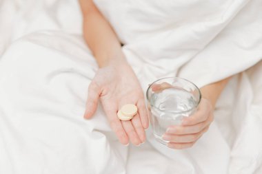 Yatağında bir bardak su ve haplarla bir bardak daha su tutan bir kadın. İlaç alma ve susuz kalma konsepti.