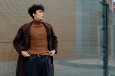 Kahverengi balıkçı yaka kazak ve koyu mavi kot pantolon giyen, elleri ceplerinde, yana doğru bakan basit moda adamı..