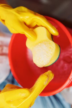 Sarı eldivenli bir kadın kırmızı kovada sünger tutuyor. Temizlik malzemeleri konsepti. Ev işleri ve hijyen konsepti. Profesyonel temizlik servisi. parlak renkler.