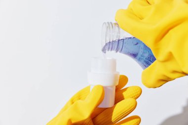 Temizlik malzemeleri konsepti - mavi sıvı şişe tutan sarı eldivenli kadın ve beyaz yüzeyde 