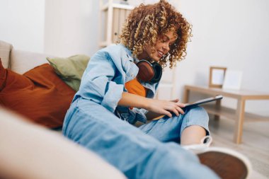 Mutlu Kadın Evde Rahatlıyor, Tablet 'te Online okuyor ve kulaklıkla müzik dinliyor, Kanepede oturuyor.