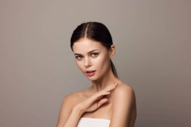 Gri bir arka planda elleri yüzü olan çekici genç bir kadın..