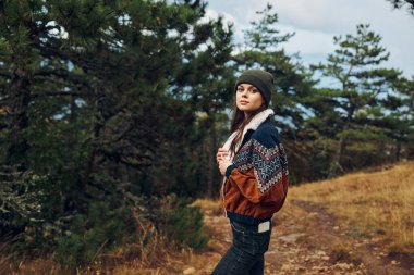 Genç bir kadın zarif şapkası ve kazağıyla ormanda doğanın huzurlu güzelliklerini keşfediyor.