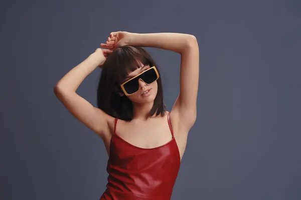 stock image Asian woman in a red dress and sunglasses posing confidently against a gray background