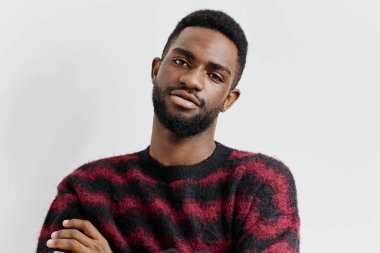 Kırmızı ve siyah süveter giyen şık genç adam, sade beyaz bir arka fona yaslanmış, öylesine bir zarafet yayıyor..