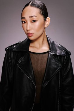 Asyalı kadın siyah deri ceket kamera grisi arka plan pozu veriyor. şık ve modaya uygun bir kadın modeli..