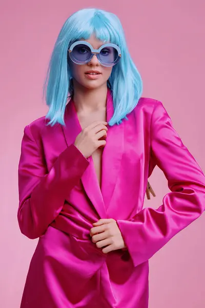 stock image Bright pink suit, blue sunglasses woman posing on a pink background with her hand on her hip and eyes closed