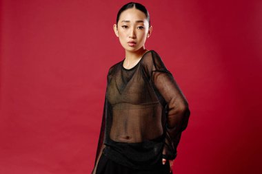 Saf bluz ve siyah etekli, elleri kalçasında, gülümseyen bir yüzle kırmızı arka planda poz veren Asyalı moda kadını..