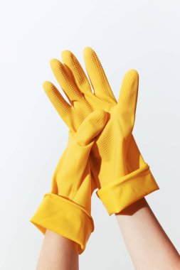 Beyaz arka planda sarı lastik eldiven tutan eller. Kopyalama alanı mevcut. Temizlik, hijyen ve ev işleri için ideal imaj.