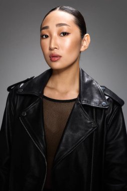Siyah deri ceketli moda Asyalı kadın gri arka planda stüdyo resmi için poz veriyor..