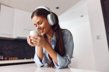 Genç bir kadın evdeki mutfağında müzik ve kahveden zevk alıyor. Rahatlatıcı bir mutluluk anı.