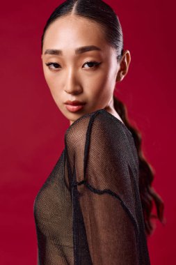 Siyah bluzlu Asyalı manken saçı at kuyruğuyla kırmızı arka plana bakıyor..