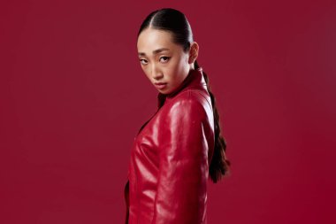 Kırmızı arka planda poz veren kırmızı deri ceketli Asyalı kadın. moda güzellik konsepti.