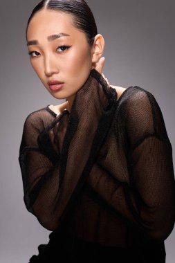 Asyalı bir kadın, katıksız bluz, poz, eller yüze. Yüzünde elleriyle kameraya poz veren genç Asyalı bir kadının şık ve şık bir portresi..