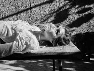 Gizemli kadın, kafası gölgelerde, masada uzanmış, entrika ve belirsizlik hissi uyandırıyor.