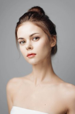 Beyaz havluyla güzel genç bir kadın gri arka planda bir stüdyoda poz veriyor..