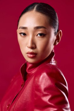 Kırmızı arka planda kırmızı deri ceketli Asyalı esmer. Asyalı bir kadının şık portresi.