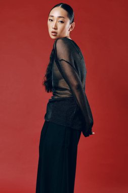 Siyah bluzlu, geniş bacaklı, elleri kalçasında kırmızı arka planda poz veren Asyalı bir kadın. şık kadın modelinin moda fotoğrafı..