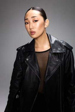 Siyah deri ceketli Asyalı kadın gri arka planda stüdyo için poz veriyor. Şık ve şık görünüm..