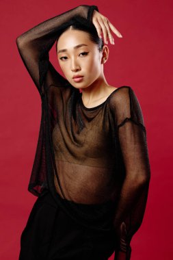 Saf bluz ve siyah pantolonlu Asyalı bir kadın moda çekimi için kırmızı arka planda poz veriyor..