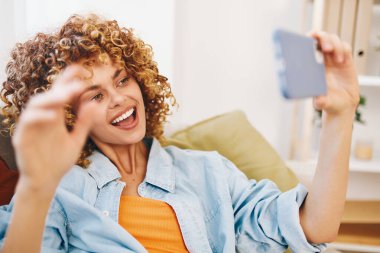 Mutlu Kadın Koltukta Oturuyor, Cep Telefonu Tutuyor ve Gülümsüyor, Çevrimiçi Oyun ve Okuma Keyifli, Selfie Çekiyor, Sohbet Ediyor: Rahat Oturma Odasında Genç Güzel Oyuncu